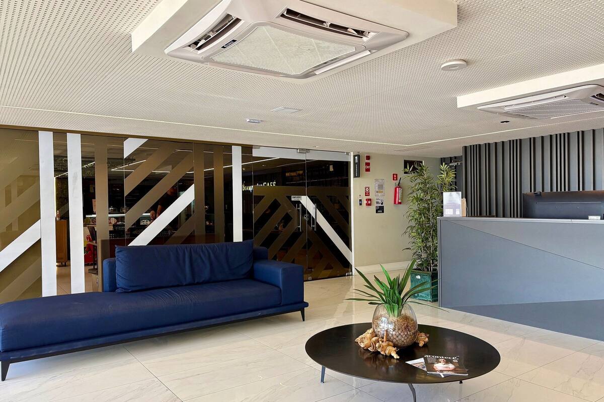 Un vestíbulo moderno con un sofá azul, una mesa redonda con un centro decorativo y un mostrador de recepción.