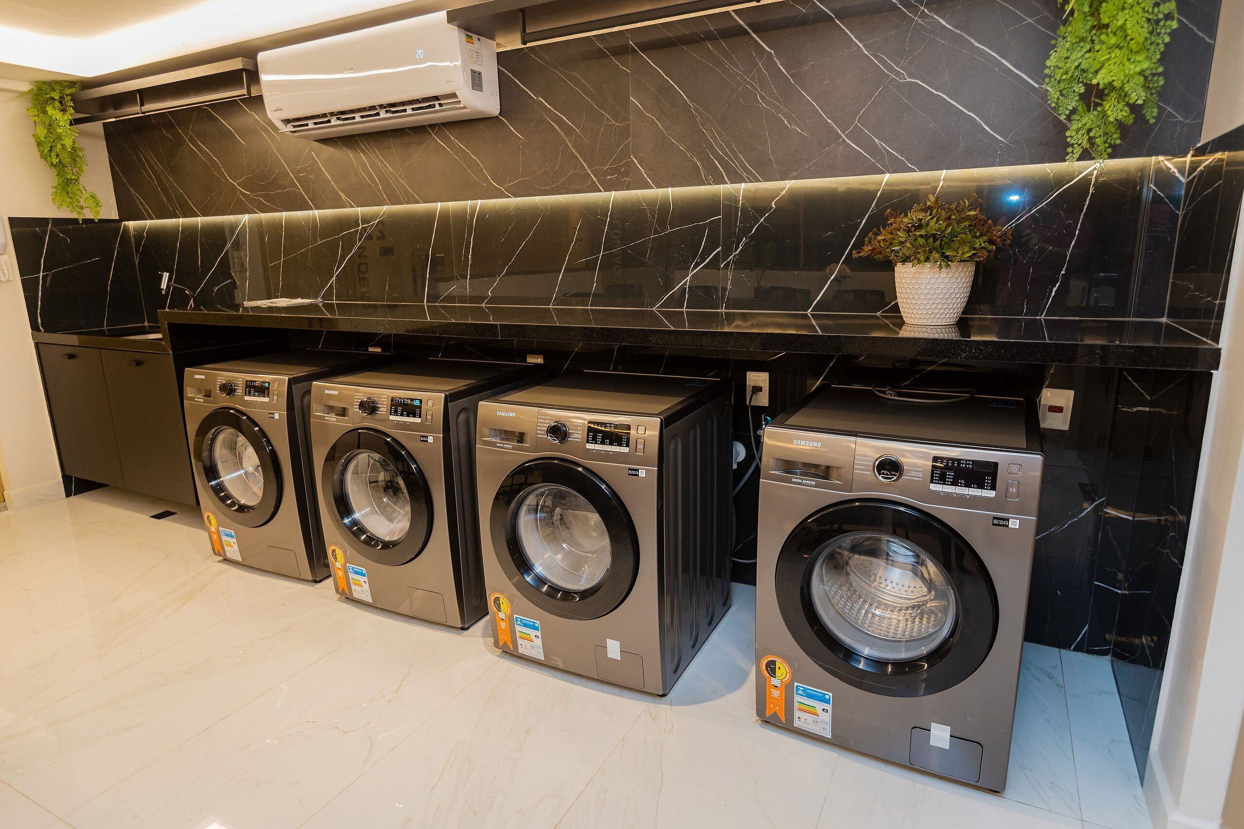A laundry area with three front-loading washers, a black marble backsplash, and an air conditioning unit.