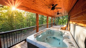 A wooden deck with a hot tub, a ceiling fan, and a view of a forest.