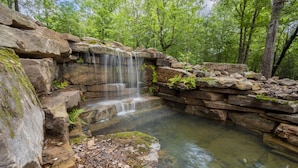 A natural rock formation with a waterfall and a clear pool.