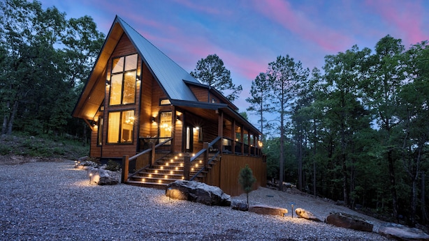 A wooden cabin with a steep roof, large windows, and a staircase leading to the entrance.
