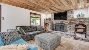 Ein gemütliches Wohnzimmer mit Kamin aus Stein, einer Ledersofa und einem Fernseher darüber montiert.