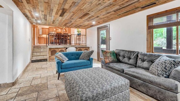 Ein geräumiger Wohnbereich mit Holzboden, einem blauen Sofa, einem grauen Sofa und einem gemusterten Hocker.