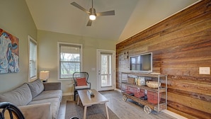 A living room with a sofa, a coffee table, a TV mounted on a wooden wall, and a small cart with baskets. - Creekside, pet friendly, wrap-around porch, minutes to downtown Hayesville! (Hayesville)