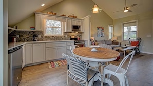 A spacious kitchen with white cabinets, a large island, and a dining area with wicker chairs. - Creekside, pet friendly, wrap-around porch, minutes to downtown Hayesville! (Hayesville)