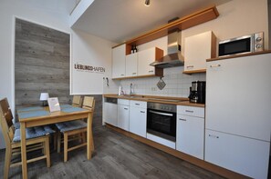 Une cuisine moderne avec des armoires blanches, un four encastré, un four à micro-ondes et une machine à café. On y trouve également un coin repas avec une table et des chaises en bois.