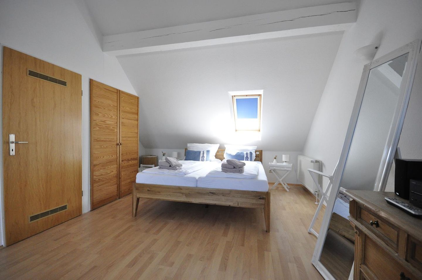 A bedroom with a wooden bed, a small bedside table, a desk, and a large mirror.
