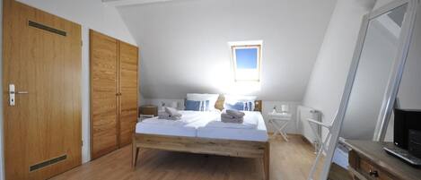 A bedroom with a wooden bed, a small bedside table, a desk, and a large mirror.