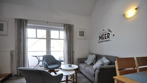Een moderne woonkamer met een grijze bank, twee fauteuils, een klein rond tafeltje en een wandlamp.