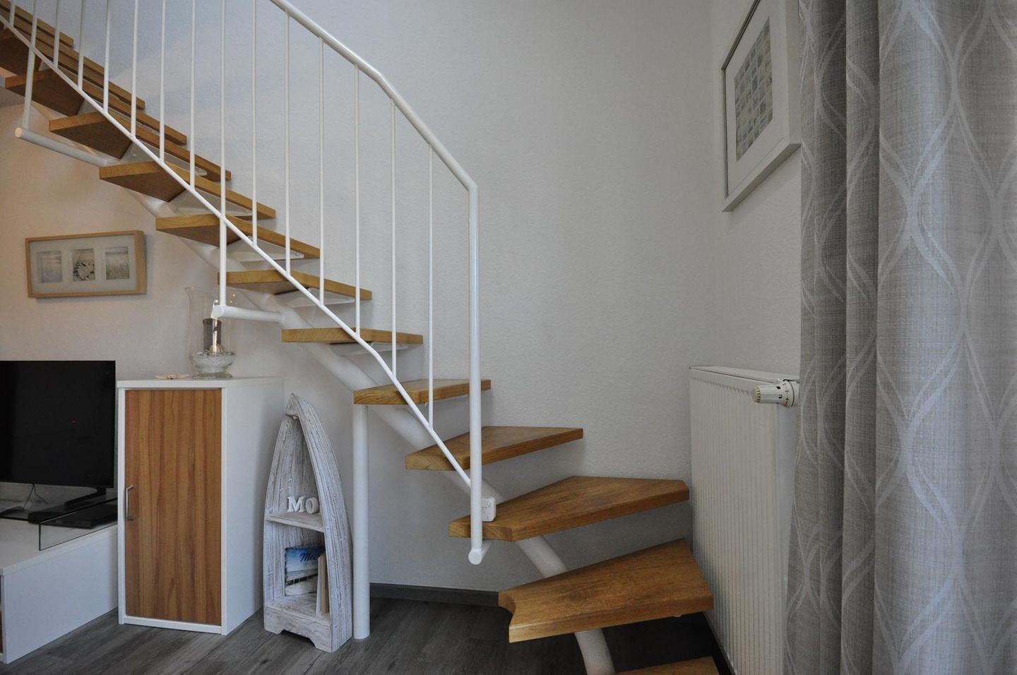 Ein modernes Interieur mit einer geschwungenen Treppe, einem Holzschrank, einem kleinen Tisch mit Lampe und einer Heizung.