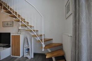Un intérieur moderne avec un escalier en colimaçon, un meuble en bois, une petite table avec une lampe et un radiateur.