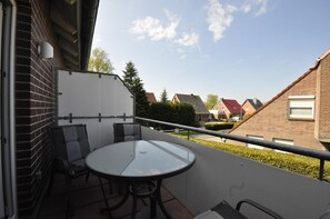 Un balcon avec une table en verre et deux chaises, un objet blanc accroché au mur, et une vue sur les maisons voisines.