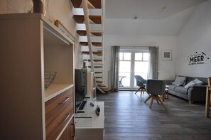 Un salon moderne avec un escalier, un canapé, un fauteuil et un coin cuisine équipé d’un réfrigérateur et de placards.