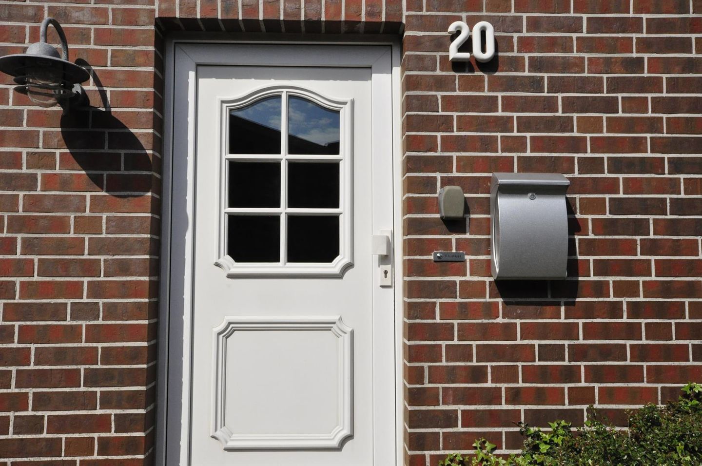 A white door with a window, a mailbox, and the number 20 on the brick wall.