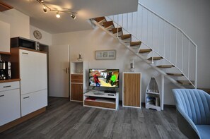 Un salon moderne doté d’un téléviseur à écran plat, de planchers en bois, d’un escalier et de meubles de rangement intégrés.