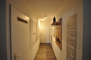 A narrow hallway with a wooden floor, a vent on the left wall, and a door at the end.