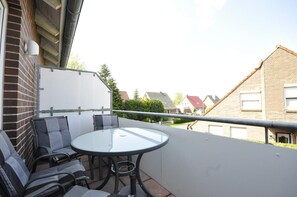 Ein Balkon mit Glastisch und Stühlen, einer weißen Wand und einem Metallgeländer.