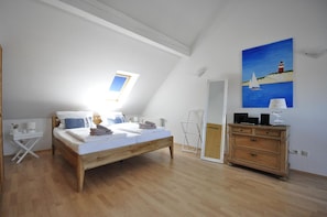 Ein Schlafzimmer mit einem hölzernen Bett, einem weißen Nachttisch, einer Kommode, einem Oberlicht und einem Gemälde eines Leuchtturms.