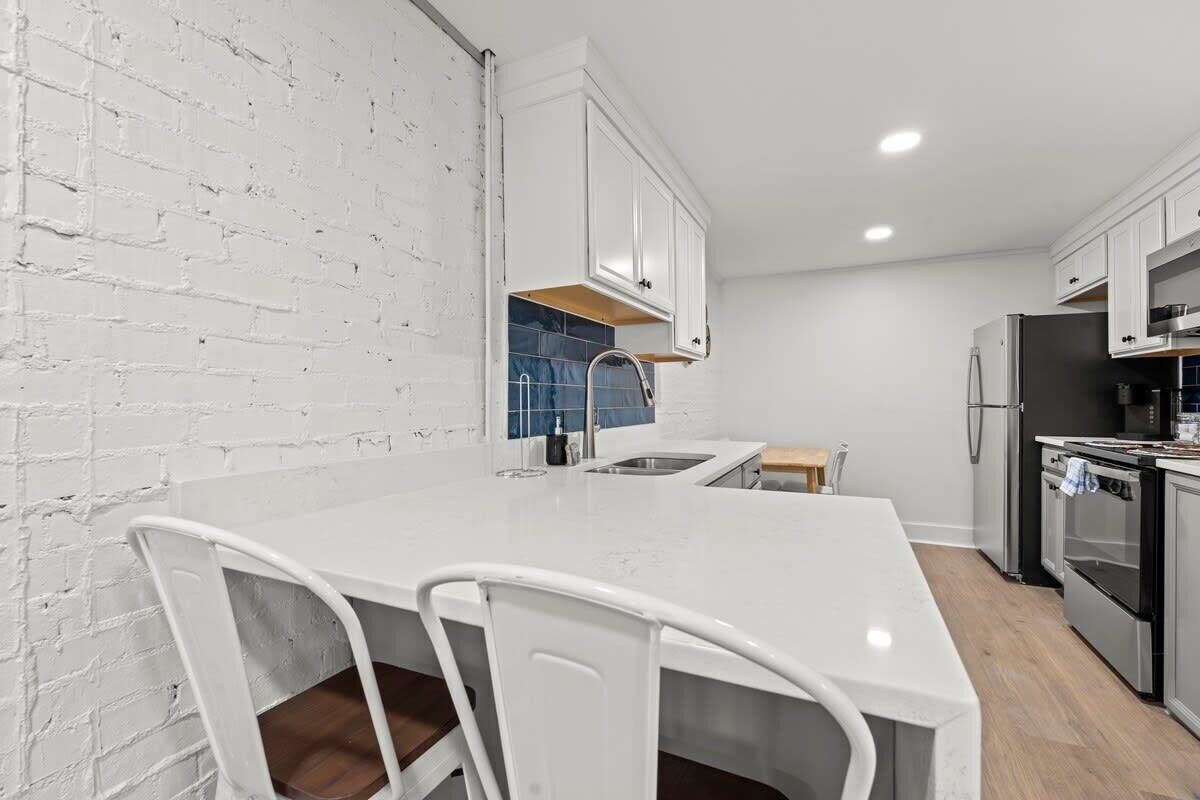 A modern kitchen with white cabinetry, a white countertop, and a brick wall.