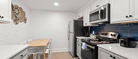 A compact kitchen with white cabinetry, a stainless steel refrigerator, a microwave, a stove, and a toaster.
