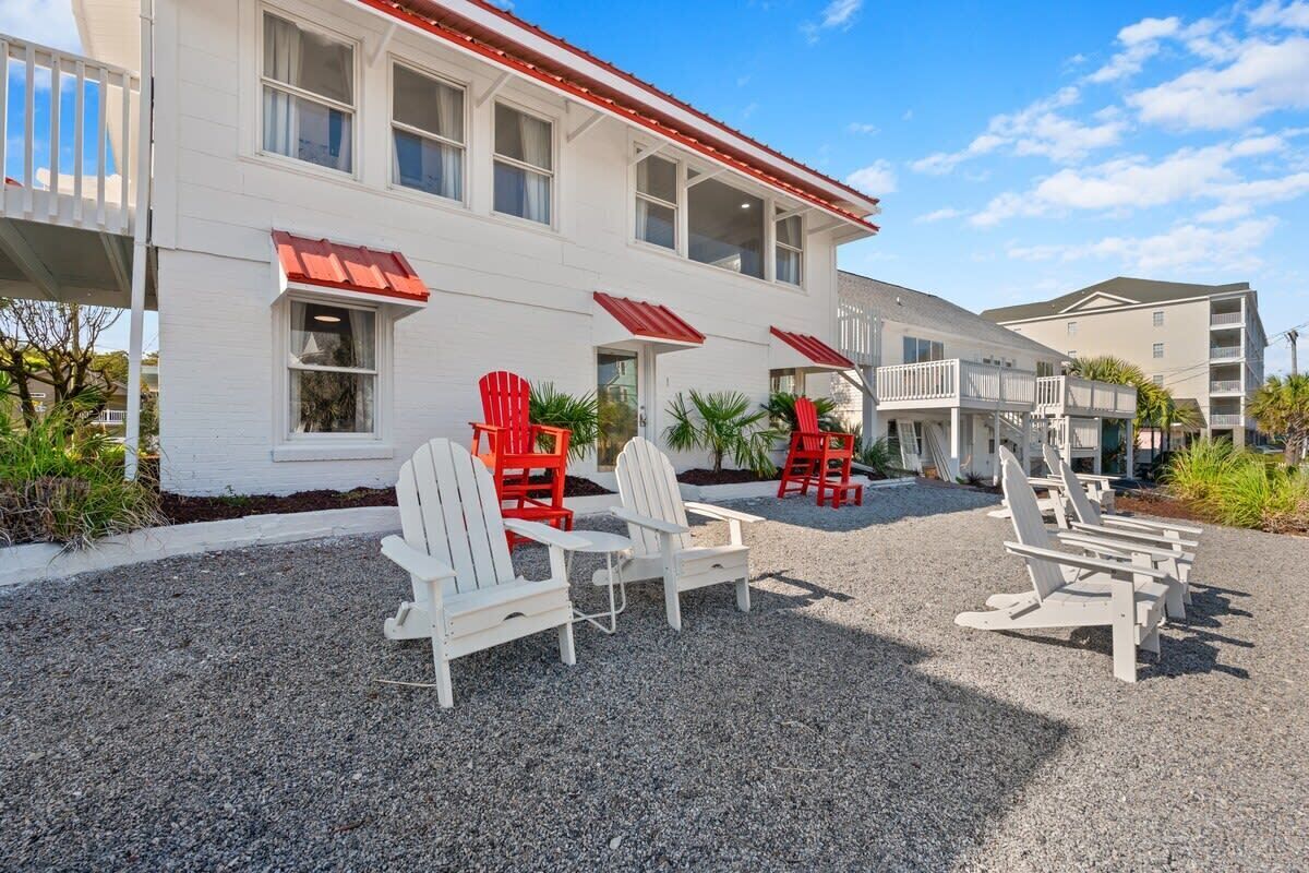 A two-story building with a red roof and white exterior. There are several Adirondack chairs arranged in the front.