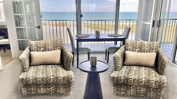 A balcony with a view of the ocean, two patterned armchairs, a small table, and a dining table with chairs. - St. Nicole Condo in Pelican Bay, Naples, Florida with Gorgeous Gulf Views (Naples)