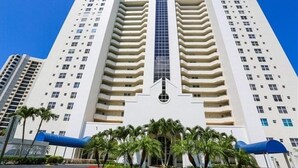 A tall, modern hotel with a central glass elevator shaft, multiple balconies, and a symmetrical facade. - St. Nicole Condo in Pelican Bay, Naples, Florida with Gorgeous Gulf Views (Naples)
