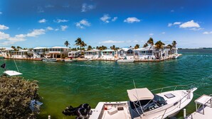 A marina with multiple boats docked, a floating structure with multiple rooms, and palm trees in the background. - Endless Water Views - Venture Out 526 (Cudjoe Key)