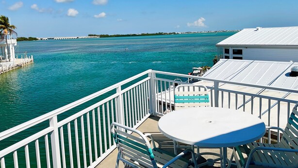 A balcony with a view of turquoise waters, a white table, and blue chairs. - Endless Water Views - Venture Out 526 (Cudjoe Key)