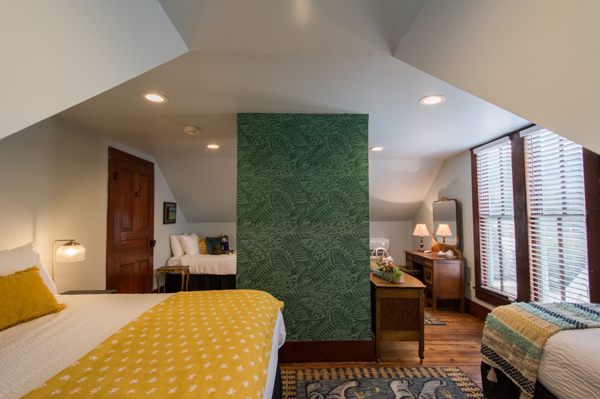 A bedroom with a bed, a desk, a chair, and a window with blinds.