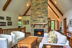Ein gemütliches Wohnzimmer mit Kamin aus Stein, weißen Ledersofas und einem Holztisch.