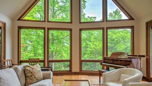 Amplia habitación con ventanas grandes, un piano, un sofá blanco y una silla.