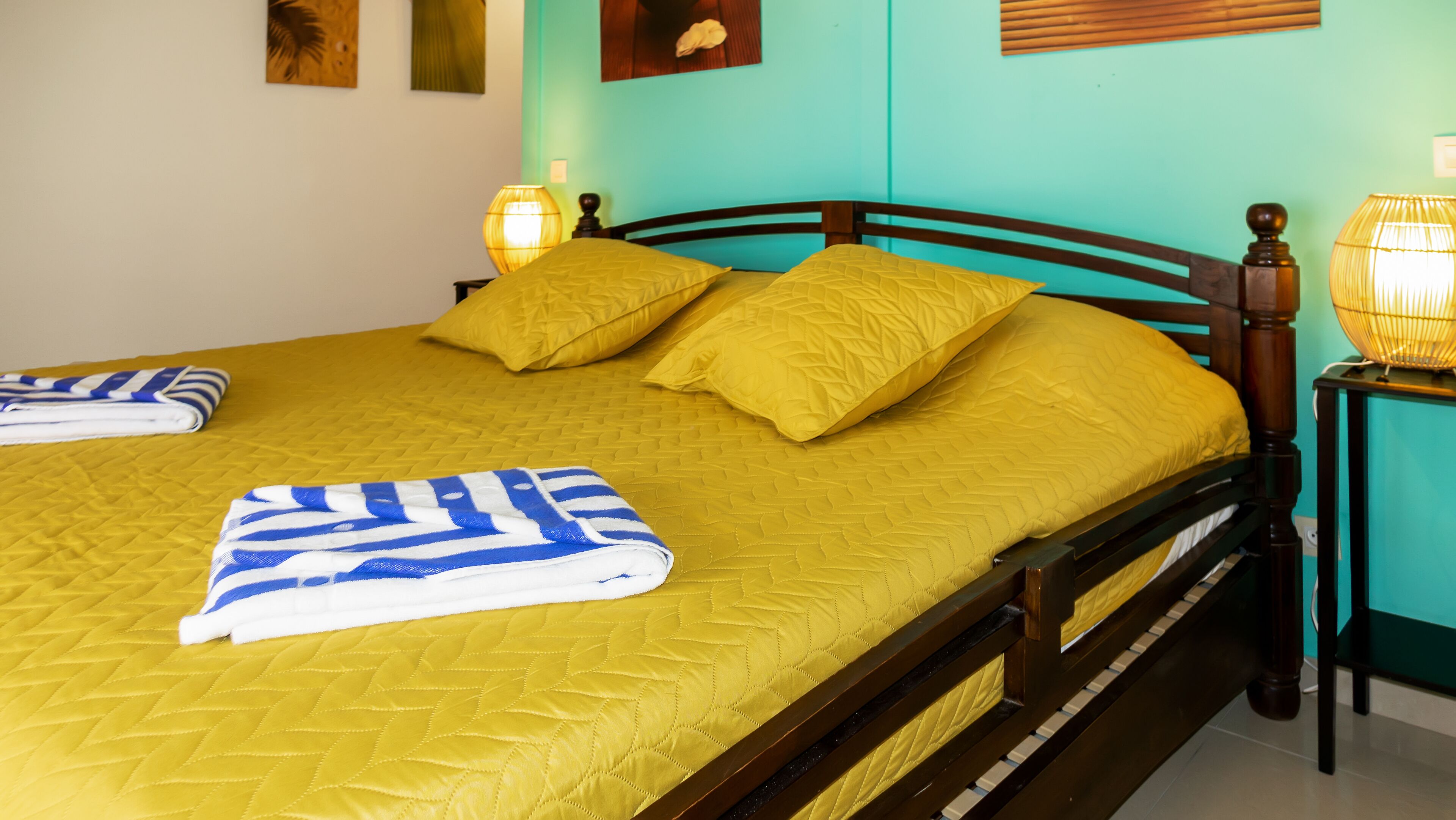 A bed with yellow bedding and pillows, a striped towel, and two bedside lamps.