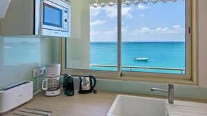 A kitchen with a coffee maker, a kettle, and a microwave. There is a window with a view of the sea and a boat. - 2 bedroom Apartment Residence Catalina (Grand-Case)