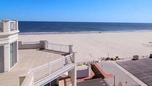 A beach view from a building with a balcony, a parking area, and a clear sky.