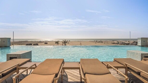 A pool with lounge chairs, a view of the beach, and a clear sky.