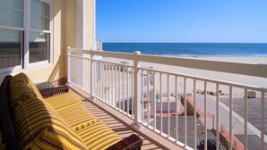 A balcony with a view of the ocean, a yellow striped sofa, and a white railing.