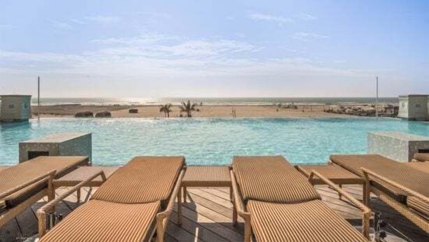 Ein Poolbereich mit Liegestühlen und Blick auf den Strand.