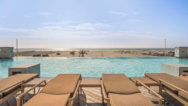 Une piscine avec des chaises longues, une vue sur la plage et un ciel dégagé.