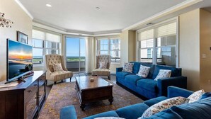 Un salon spacieux avec un grand téléviseur à écran plat, deux fauteuils, un canapé bleu et une table basse.
