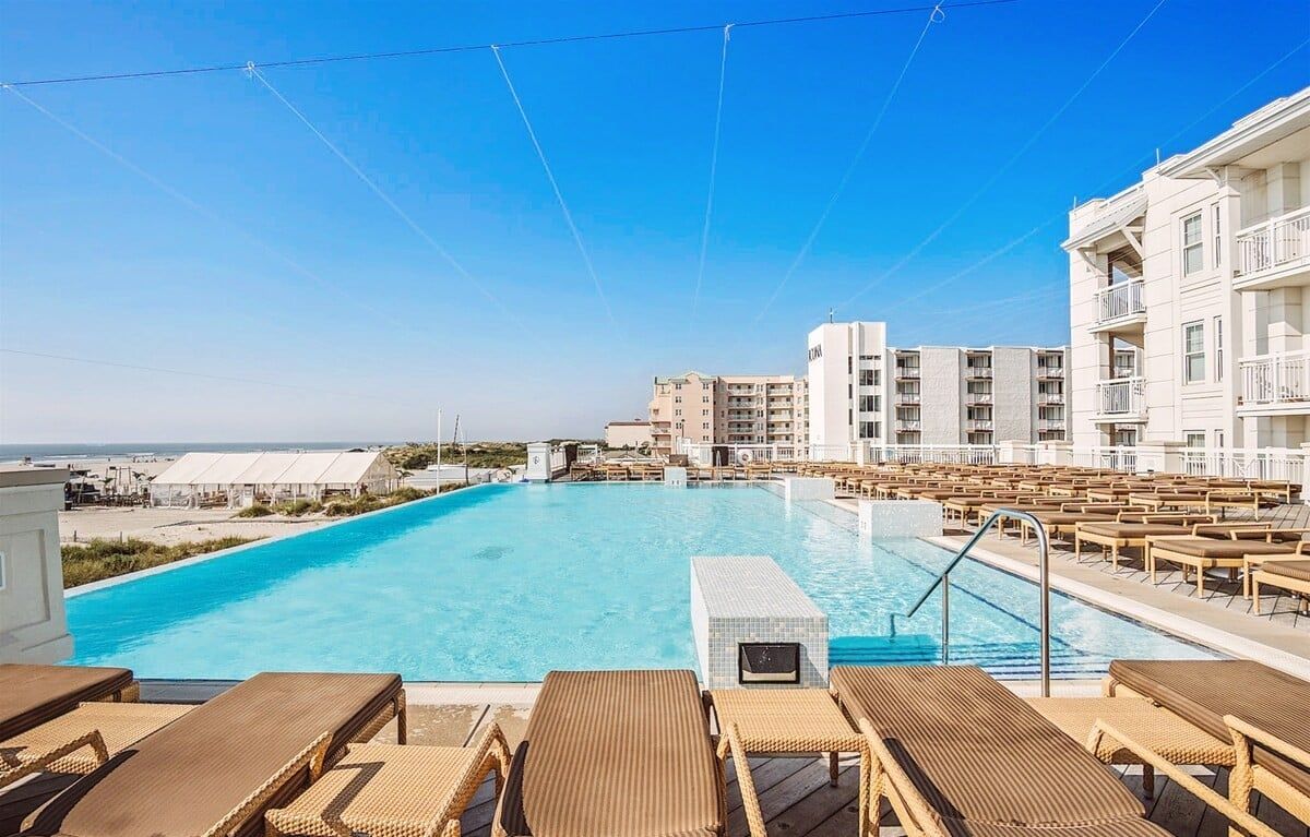 Una piscina con sillas de descanso y vistas a una playa y edificios.