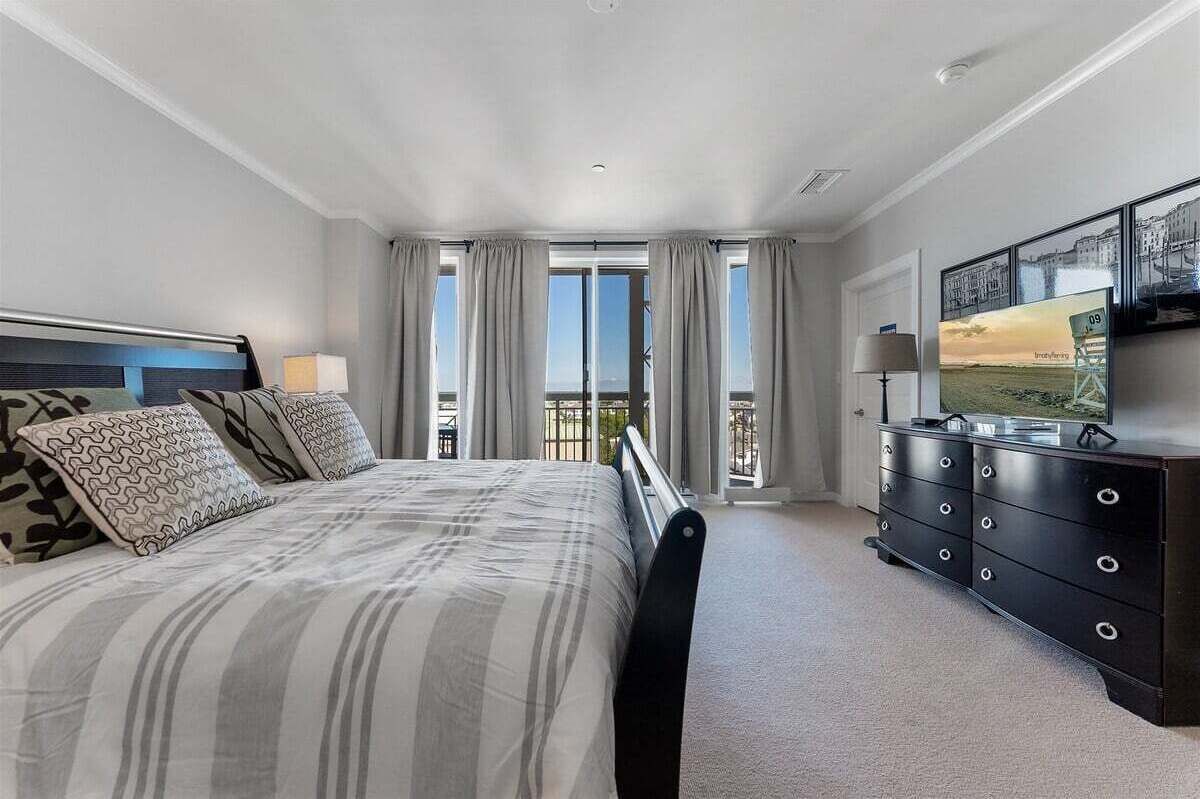 Una camera da letto con un letto, una cassettiera, una TV e un balcone con tende.