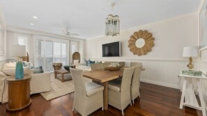 Un salon spacieux avec une table à manger en bois, des sièges confortables, un téléviseur à écran plat et un miroir décoratif au mur.