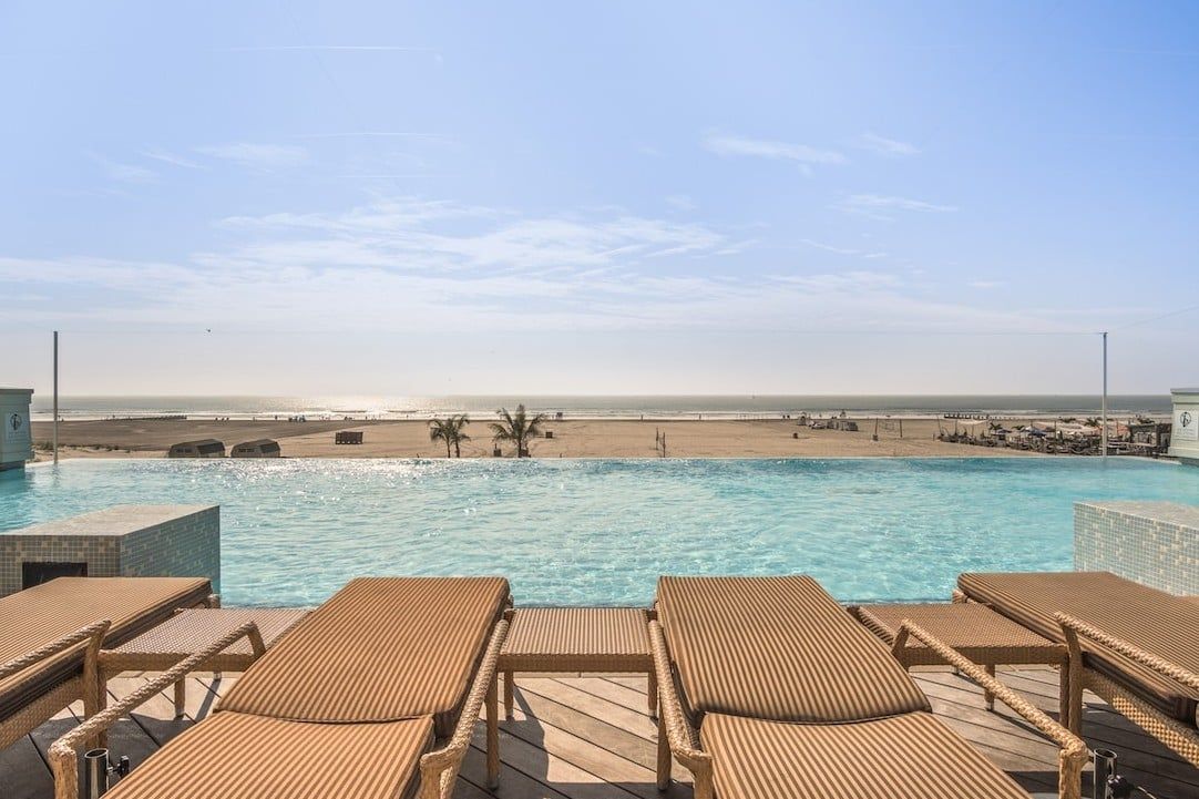 A poolside area with lounge chairs, a view of the beach, and a clear sky.