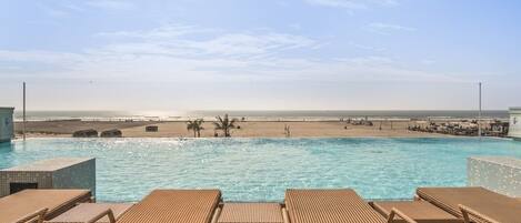 A poolside area with lounge chairs, a view of the beach, and a clear sky.