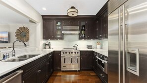 Una cocina moderna con gabinetes oscuros, electrodomésticos de acero inoxidable y una encimera blanca.