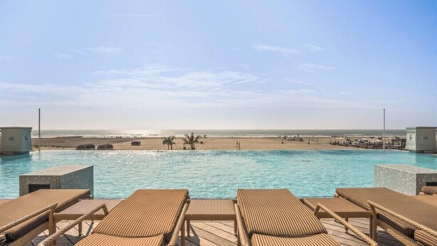Une piscine avec des chaises longues, une vue sur la plage et un ciel dégagé.