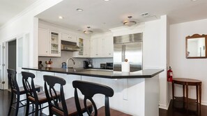 A modern kitchen with white cabinetry, a stainless steel refrigerator, and a bar area with stools.