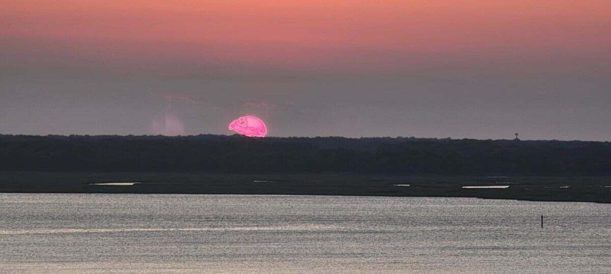 A sunset over a body of water with a distant shoreline.