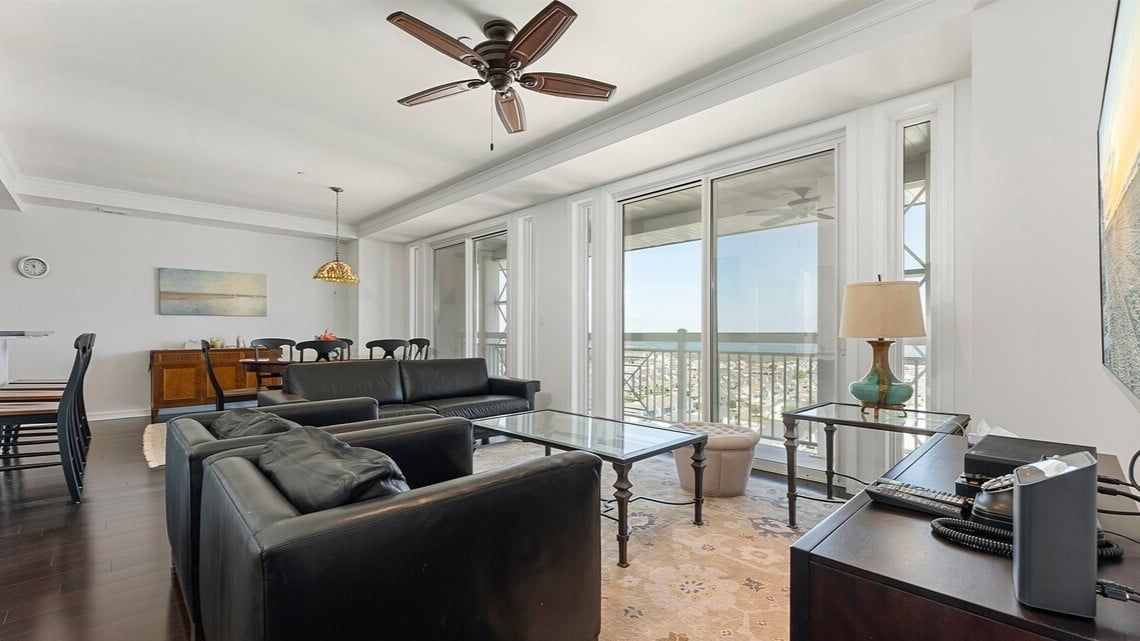 A spacious living room with a glass coffee table, leather sofas, a dining area with a wooden table, and a balcony with a view.